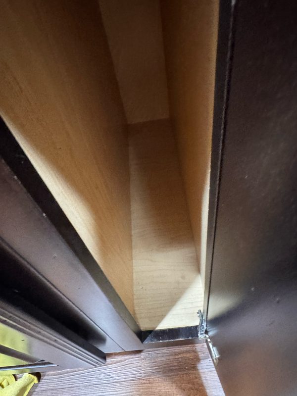 The same cabinet corner after cleaning, with the residue gone and bare pale wood on both panels.