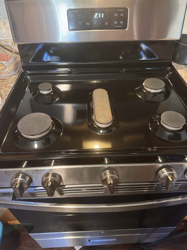 The same gas cooktop after cleaning, with the black surface wiped clear of debris and the burner caps clean.