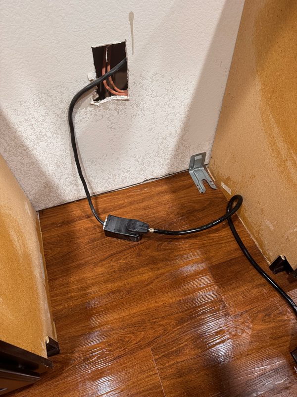 The same gap behind the appliance after cleaning, with the debris removed and the wood floor washed and still damp.