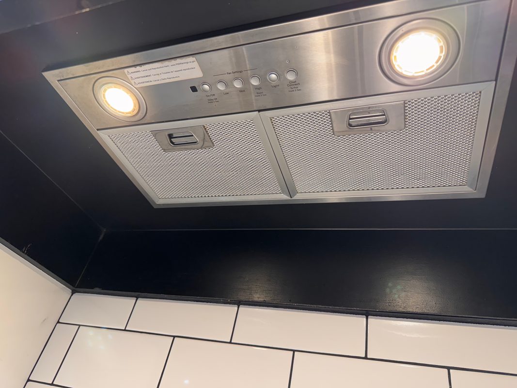 The same range hood after cleaning, seen from a little to the left, with both filters back to bare silver mesh and its two lights on.