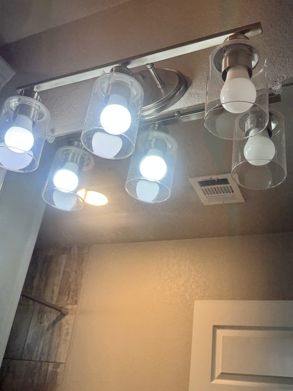 Looking up at a bathroom vanity light with six clear glass shades before cleaning, with fine specks of dust and spots across the glass.